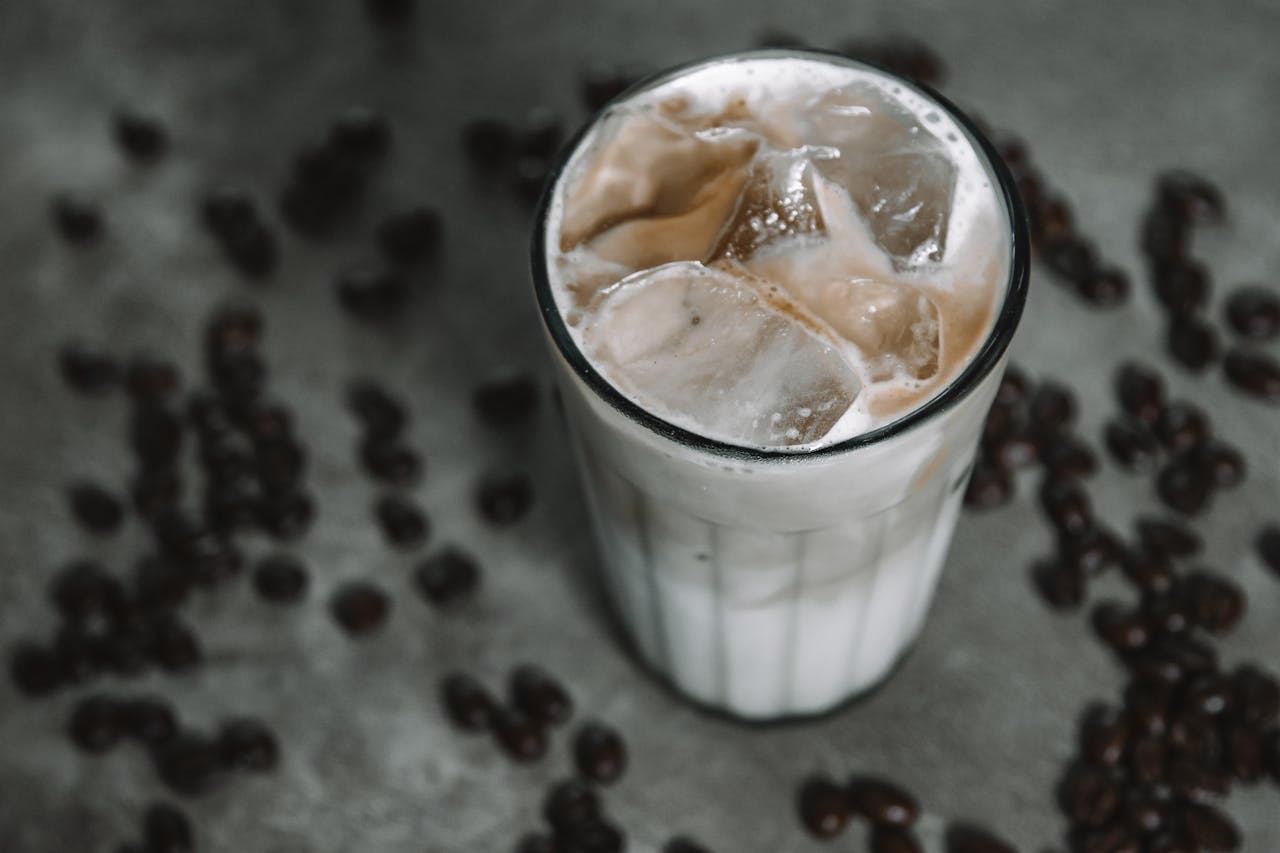 Close-up view of a creamy iced coffee with ice cubes, surrounded by coffee beans.